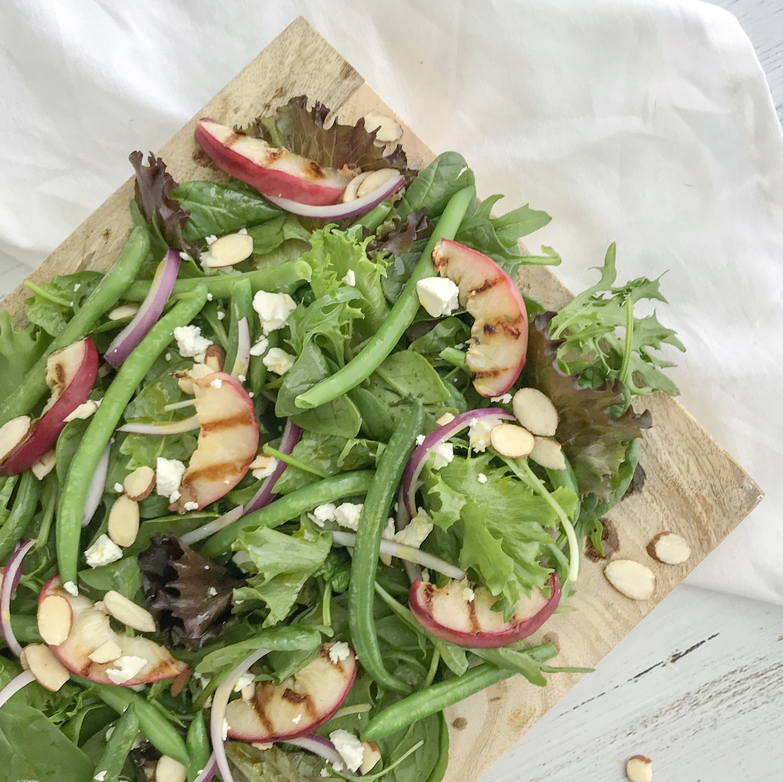 Close up of grilled peach, green bean and almond salad with red onions and crumbled feta