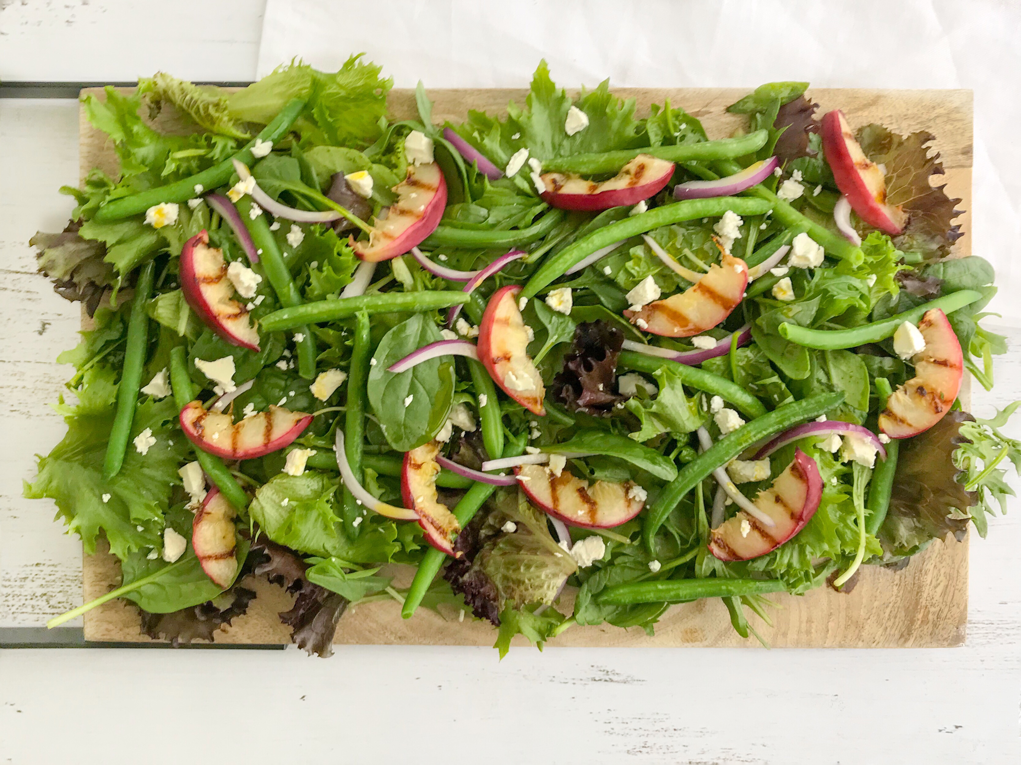 Grilled peach, green bean and almond salad spread out on a wooden platter 